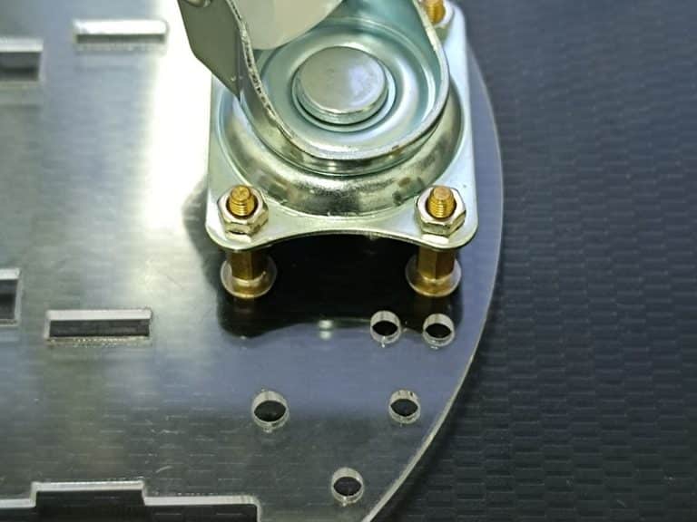 Zoom sur la fixation d'une roue folle au châssis inférieur du EasyRobot V3, illustrant le serrage des vis et les entretoises utilisées.